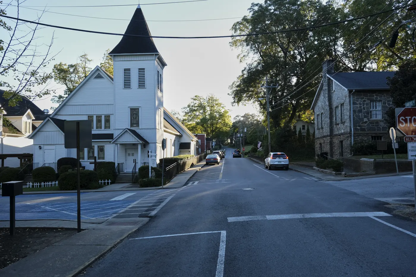 Small-town intersection with a white steepled church on one corner and a stone building with a stop sign on the other