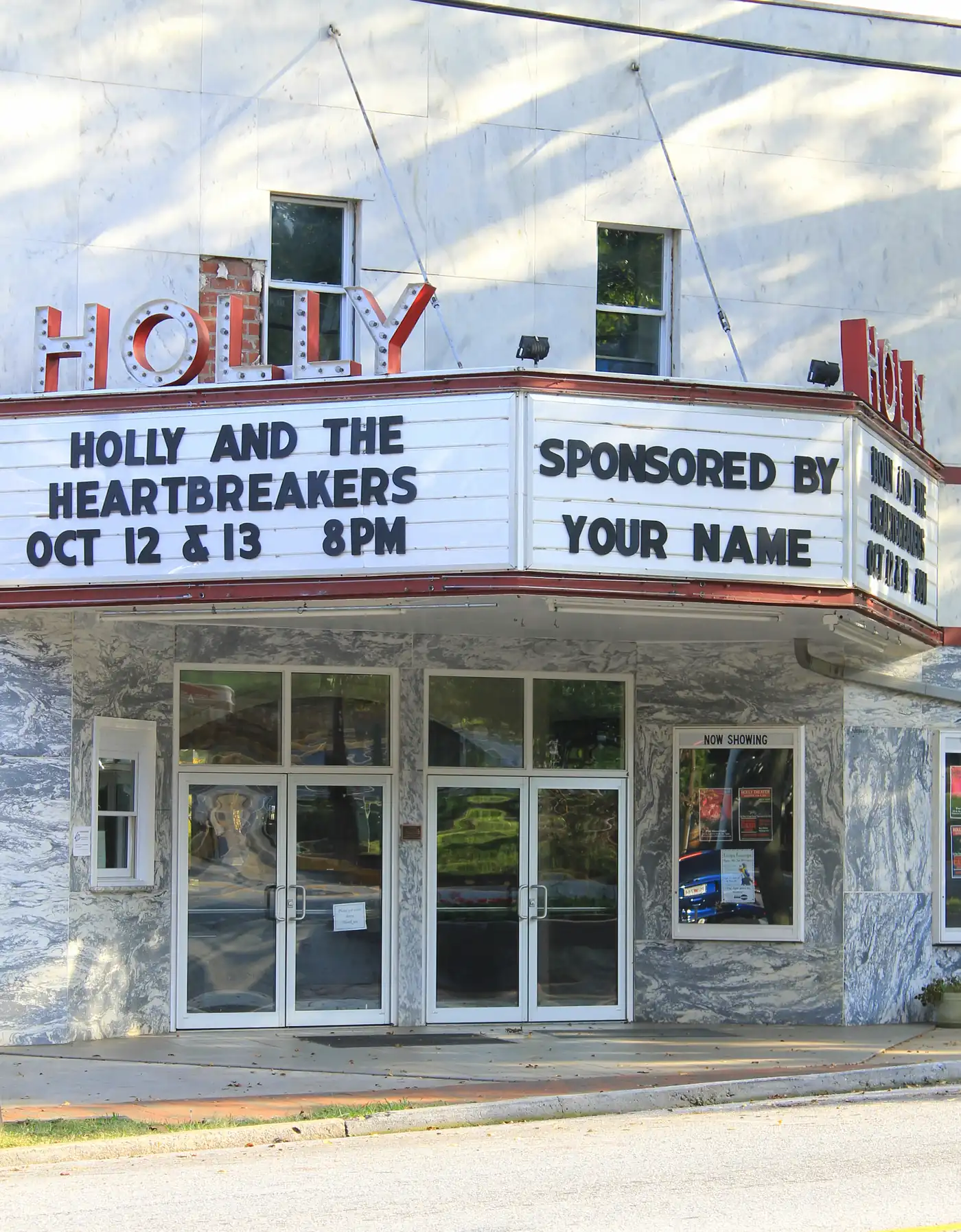 Marble theater front with red HOLLY letters and a white marquee above glass entry doors