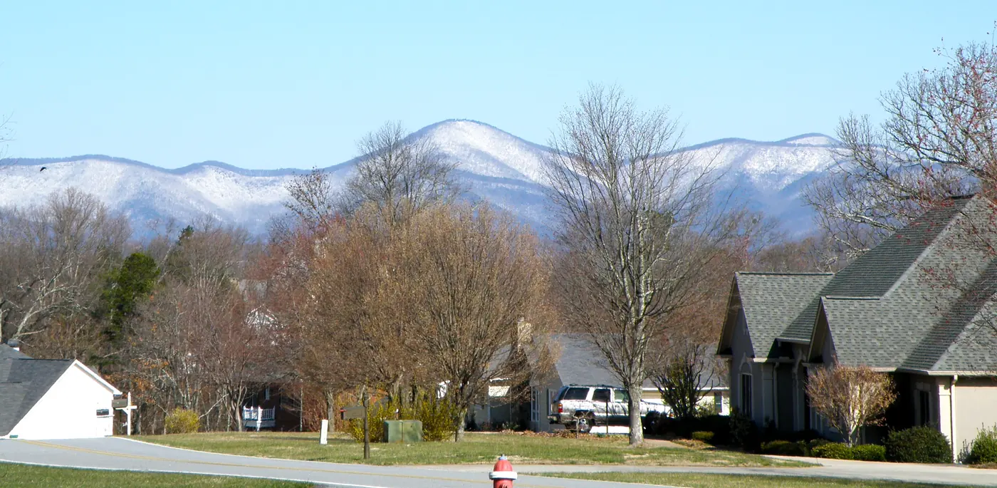 Neighborhood street with houses and bare trees, a fire hydrant in front, and snow-dusted mountains on the horizon
